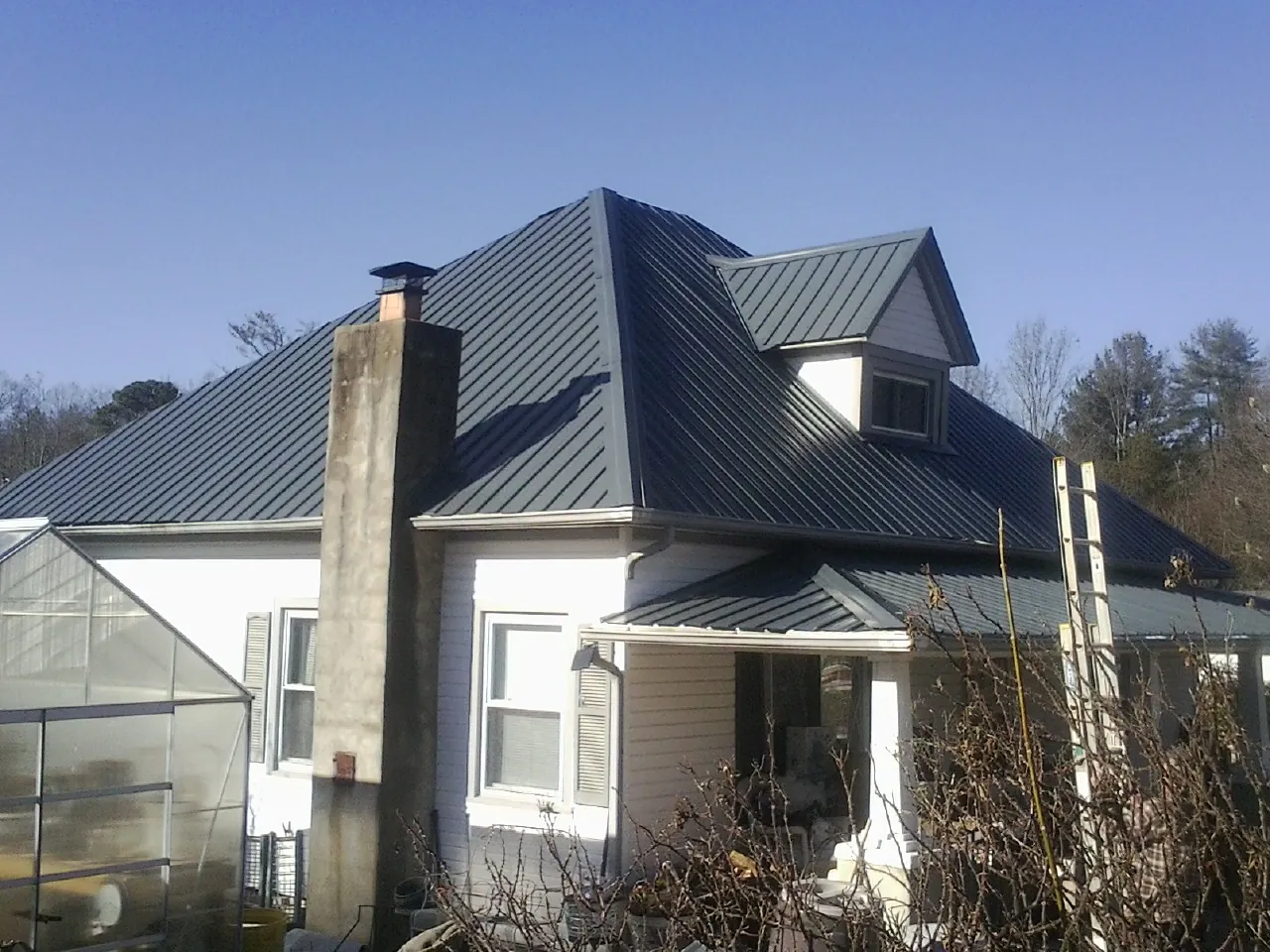 Dark blue standing seam metal roof on a white farmhouse with dormer — Slate & Tile Roof Repair by Roofing Brothers in Siloam