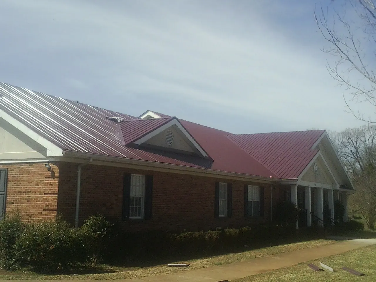 Red metal roof with gabled entries on a long brick building, from a Hail Damage Roof Repair job in Siloam