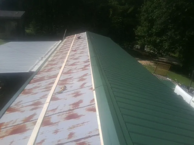 Old rusted panels beside newly installed green metal roofing — Wind Damage Roof Repair by Roofing Brothers in Siloam