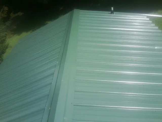 New green metal panels meeting at the ridge of a roof — Flat Roof Repair work by our crew in Siloam