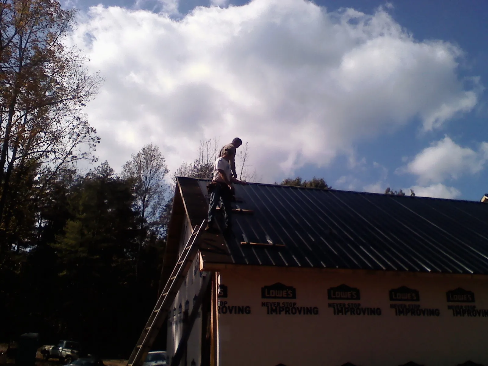 Roofer fastening dark metal panels high against a cloudy sky, from a Roof Inspection job in Siloam