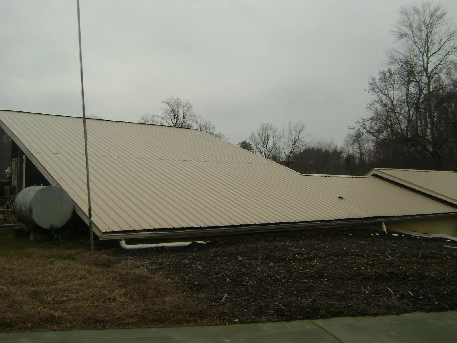 Wide tan metal roof plane seen from the ground beside a propane tank in Siloam