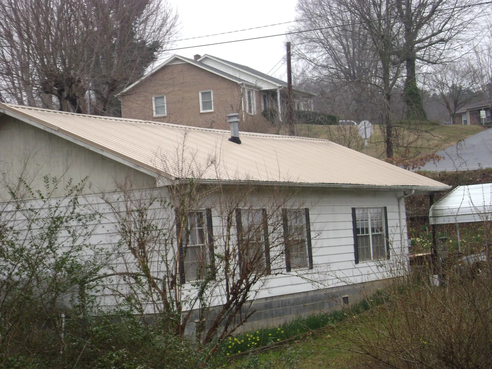 Tan metal roof on a white sided house set into a hillside — Commercial Roofing by Roofing Brothers in Siloam